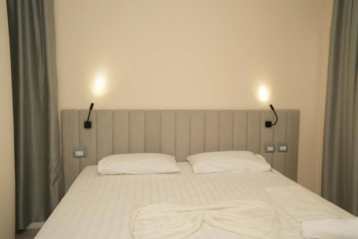 Una camera d'albergo con un letto, due lampade ai comodini e una testiera.