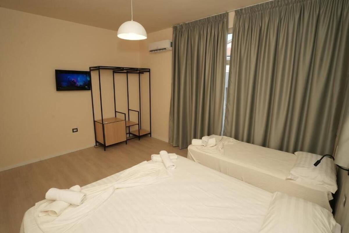 Una camera d'albergo con due letti, una zona salotto, una TV e una finestra con tende.