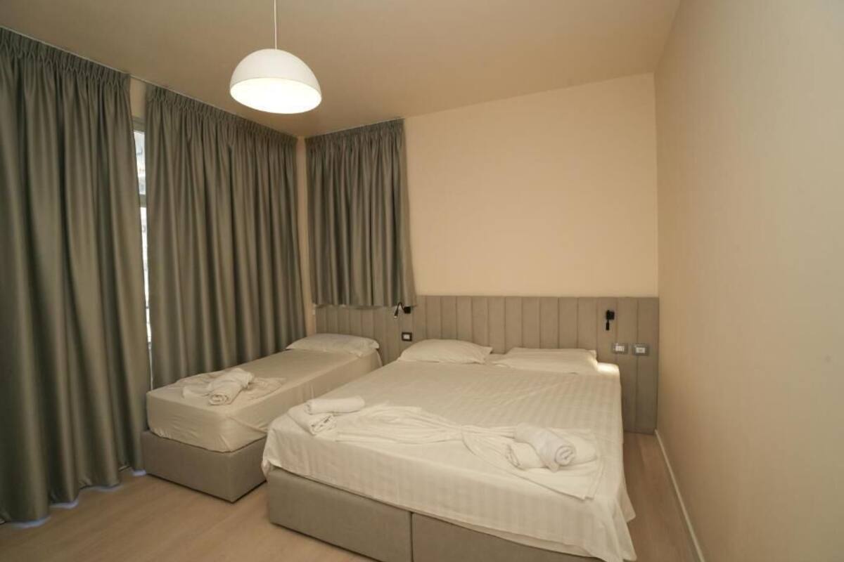 Una camera d'albergo con due letti, un'ampia finestra con tende, un lampadario e un pavimento in legno.