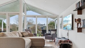 Un salon moderne avec un canapé d’angle, une petite table et un téléviseur. Une grande fenêtre offre une vue sur l’extérieur.