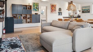 Un salon moderne avec un canapé d’angle gris, une bibliothèque grise foncé et un coin repas comprenant des chaises et une table en bois.