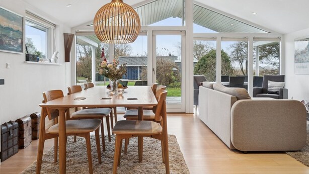 Un vaste espace dédié à la salle à manger, avec une table et des chaises en bois, un grand lustre suspendu et une vue sur l’extérieur grâce à de grandes fenêtres.