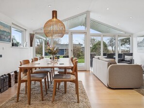 Un comedor amplio con una mesa y sillas de madera, una lámpara colgante grande y vistas al exterior a través de ventanas amplias.