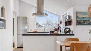 Une cuisine moderne dotée d’un grand îlot central, d’appareils électroménagers en acier inoxydable et offrant une vue sur l’extérieur.