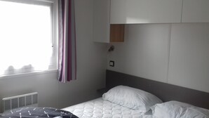 A bedroom with a bed, a window with curtains, a radiator, and a wall-mounted shelf.