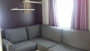 A gray sectional sofa with a wooden shelf above it.