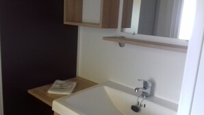 A bathroom with a white sink, a mirror above it, and a small wooden shelf.