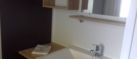 A bathroom with a white sink, a mirror above it, and a small wooden shelf.