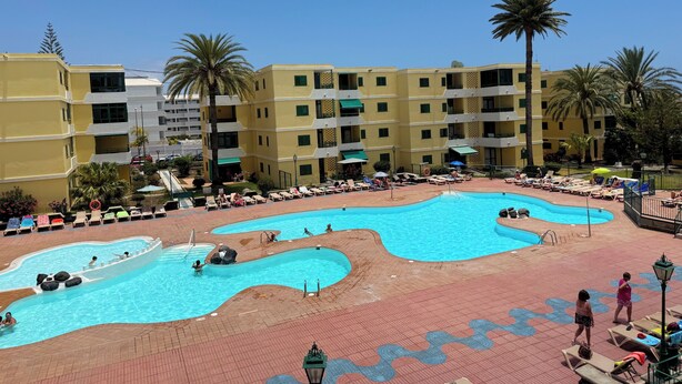 Ein Resort mit mehreren Schwimmbecken, Liegestühlen und Palmen.
