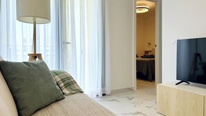 Ein modernes Wohnzimmer mit einer Couch, einer Lampe, einem Fernseher und Blick durch transparente Vorhänge.