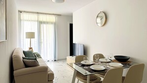 Ein modernes Wohnzimmer mit einer Couch, einem Glastisch für vier Personen und einem Fernseher.