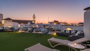 Una terraza en la azotea con césped artificial, sillones de descanso y un espacio de estar con cojines.