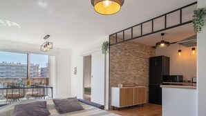 A modern apartment with a large bed, a dining area, a kitchen, and a balcony with a view of buildings. - Arcachon Marines by Interhome (Arcachon)