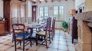 A dining room with a long table, wooden chairs, a clock, and a stone fireplace. - Ti Breizh by Interhome (Guimaëc)