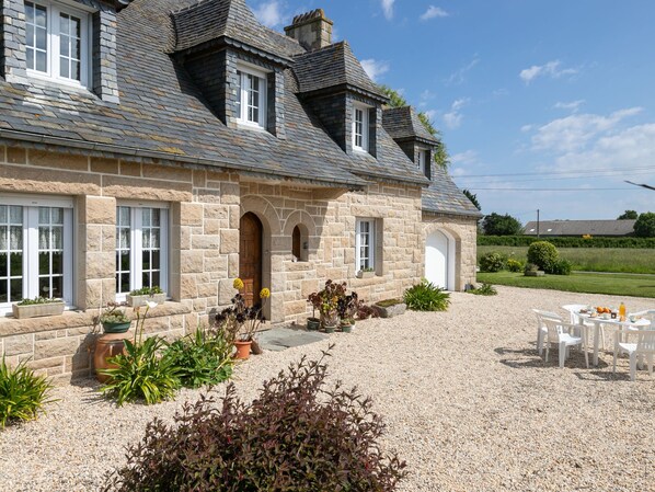 A stone house with a gravel driveway, outdoor seating, and a garden.
