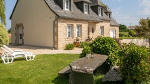 A stone house with a sloped roof and a small garden area with a bench and a table. - Ti Breizh by Interhome (Guimaëc)
