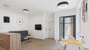 En moderne stue med en grå sofa, et træsofabord, et tv ophængt på væggen og et spiseområde med et hvidt bord og stole.
