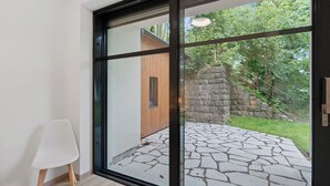 Et moderne interiør med en stor glasdør, der fører ud til en udendørs sten terrasse og en trækonstruktion.