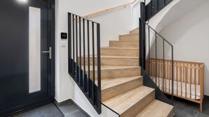 Un escalier moderne avec des marches en bois et des rampes en métal noir, menant à une chambre à coucher dotée d’une tête de lit en bois.