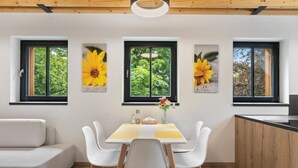 Une cuisine moderne avec un coin repas, un plafond en bois et de grandes fenêtres ornées de peintures florales.