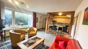 Un espacio habitable compacto con sofá, una mesa de centro, televisor y una zona de cocina con taburetes de bar.