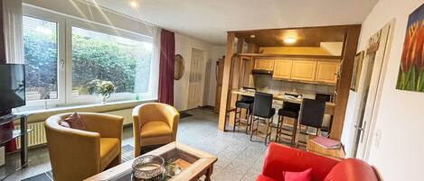 A compact living space with a sofa, a coffee table, a TV, and a kitchen area with bar stools.