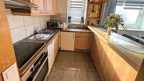 A compact kitchen with wooden cabinets, a microwave, toaster, sink, and a window with curtains. - Fewo 4 in ruhigem Haus by Interhome (Sylt)