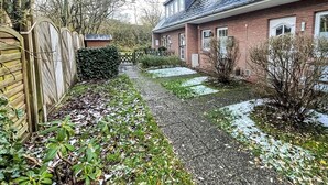 A residential property with a paved driveway, a wooden fence, and a brick house with multiple windows. - Vacation home Tinnum by Interhome (Sylt)