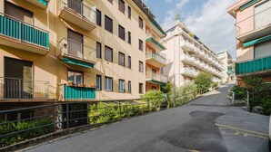 Un immeuble résidentiel à plusieurs étages, doté de balcons, situé le long d’une rue pavée, sous un ciel dégagé.