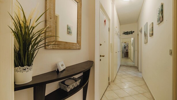Un couloir avec une console sombre, une plante en pot, un miroir et un thermostat.