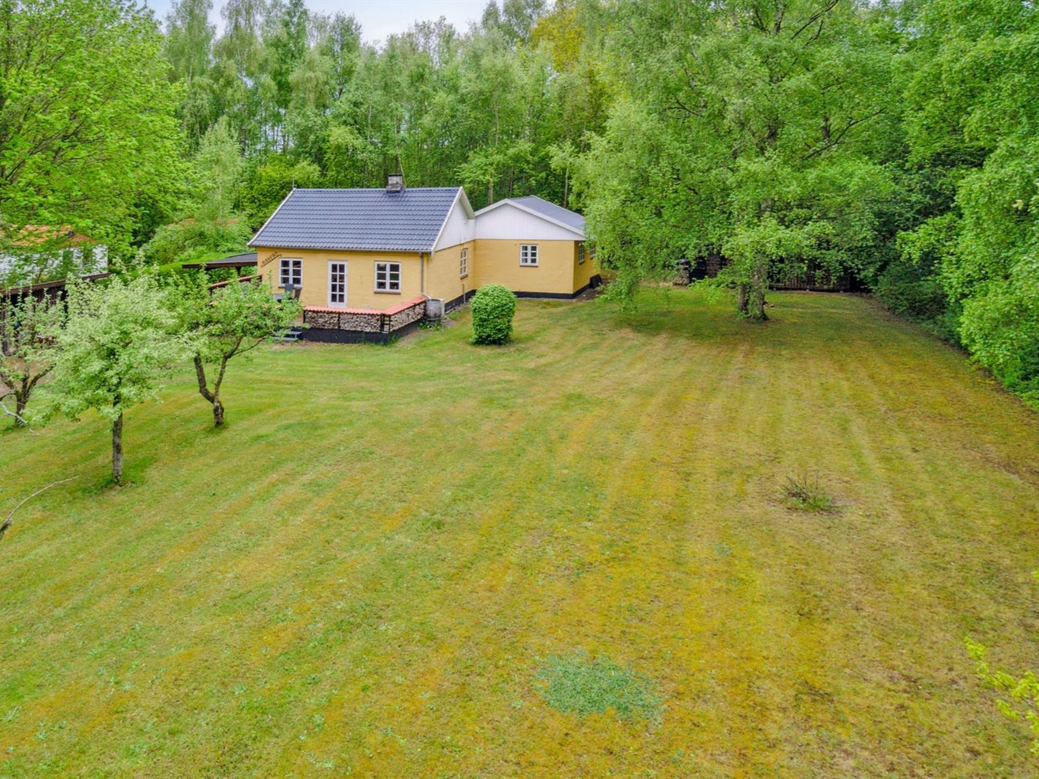 A two-story house with a fenced yard, surrounded by dense trees.