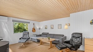 A modern living room with a wooden ceiling, a grey sofa, a black leather chair, a small table, and a guitar. - "Eine" -  from the sea by Interhome (Hals)