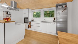 A modern kitchen with white cabinetry, a stainless steel refrigerator, and a wooden ceiling. - "Eine" -  from the sea by Interhome (Hals)
