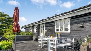 Een houten terras met een tafel, stoelen, een bankje en potten met planten.