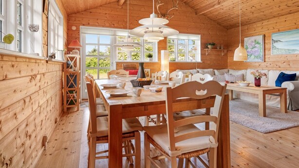 Een gezellig cabin interieur met een houten eethoek, een bank en een groot raam met uitzicht op groen.