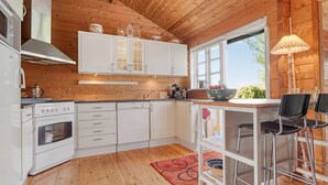 Een moderne keuken met witte kasten, een houten plafond en een groot raam dat natuurlijk licht binnenlaat.