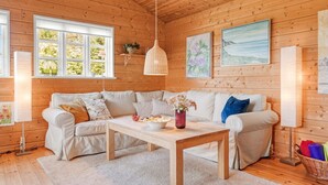 Een gezellig chaletinterieur met houten plafond, een zithoek, een tafel met vaas en kunstwerken aan de muren.