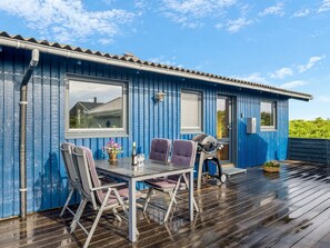 Ein blaues Gebäude mit einer Terrasse, einem Tisch mit Stühlen, einem Grill und einem Fenster.