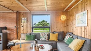 A cozy room with a sofa, a coffee table, a fireplace, and a large window offering a view of greenery.