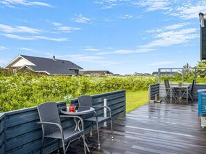 Eine Holzdielen-Terrasse mit Gartenmöbeln, Blick auf eine Wohngegend und einen klaren Himmel.