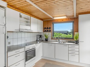 Une cuisine moderne avec des meubles blancs, un four encastrĂ©, une machine Ă cafĂ© et une fenĂȘtre donnant sur un paysage verdoyant.