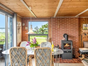 Une pièce chaleureuse avec une cheminée en briques, une table à manger avec des chaises et une grande fenêtre donnant sur un paysage verdoyant.