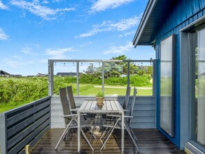Eine überdachte Terrasse mit Tisch, Stühlen und einer Zimmerpflanze, mit Blick auf eine grüne Landschaft.