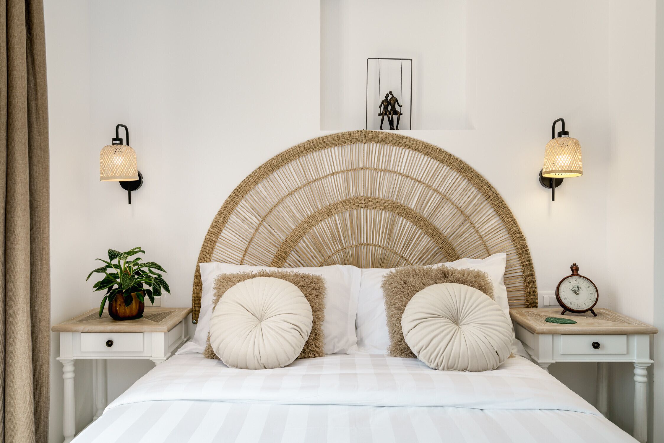 Ein Bett mit einem gewobenen Kopfteil, zwei Nachttische mit Wandlampen, ein Topf mit Pflanze und ein gerahmtes Bild an der Wand.