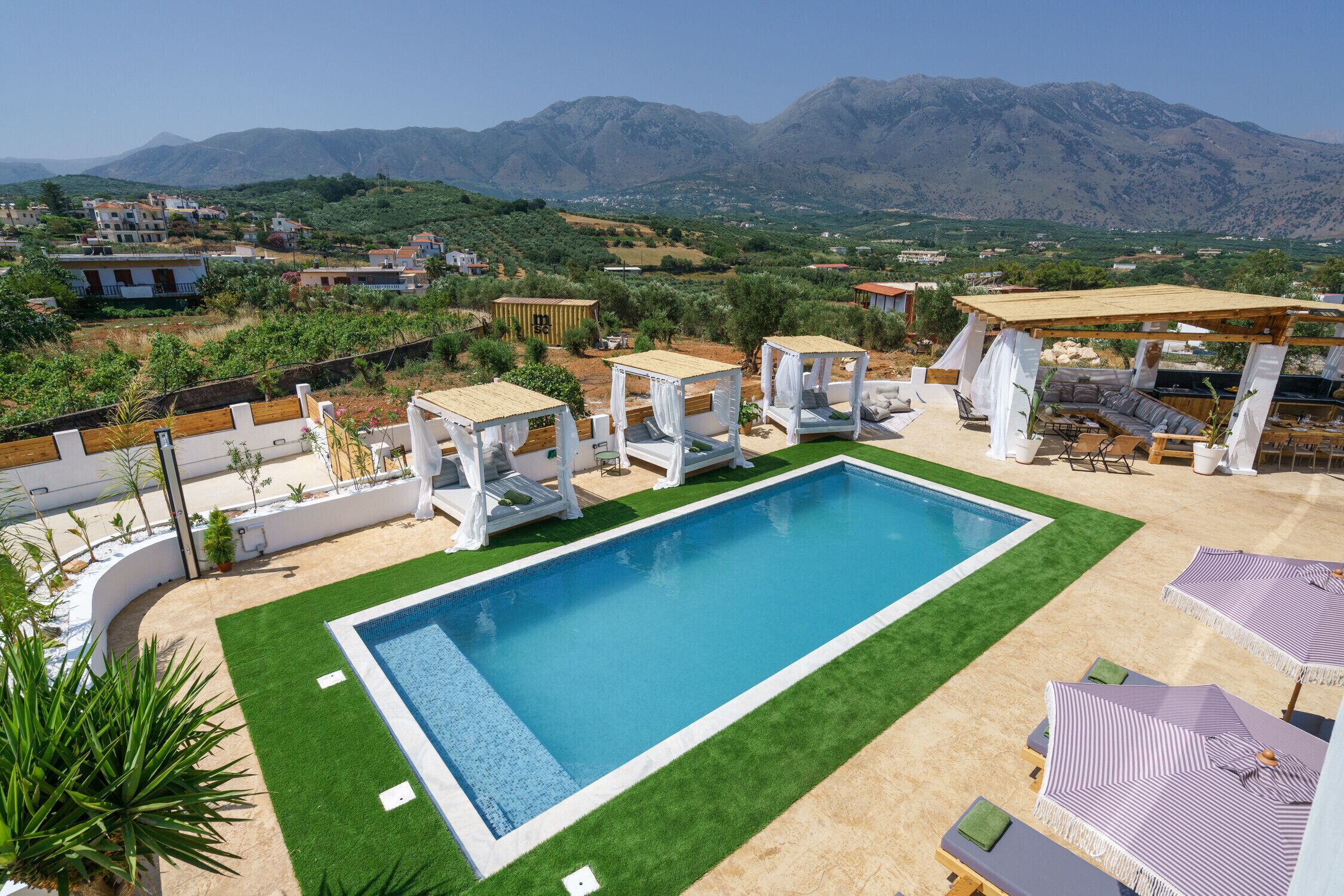 Ein rechteckiger Pool mit einer umlaufenden Liegefläche, weißen Pergolen und Lounges mit gestreiften Sonnenschirmen.