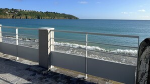 Une vue sur la côte, avec une balustrade, un ciel dégagé et une ligne de rivage lointaine où l’on aperçoit des bâtiments.