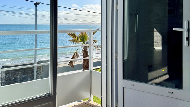 Une pièce dotée d’une porte-fenêtre coulissante donnant sur un balcon avec vue sur l’océan.