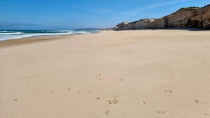 Een breed zandstrand met aan de ene kant een rotsklif en aan de andere kant de oceaan.