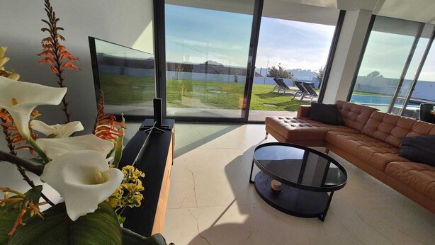 Een moderne woonkamer met een grote glazen deur die uitkomt op een balkon met uitzicht op zee.