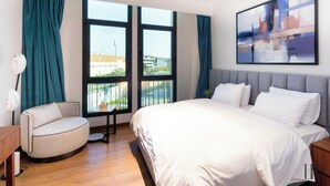A modern hotel room with a large bed, a round armchair, and a view of the city through large windows. - Easy Rental/ Serviced Apartment In CFC New Cairo (NEW Cairo Governorate)